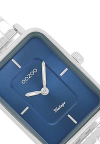 Montre en acier inoxydable argenté avec un cadran bleu rectangulaire. Présente des index horaires minimalistes, des aiguilles argentées et le texte « OOZOO Vintage ». 
