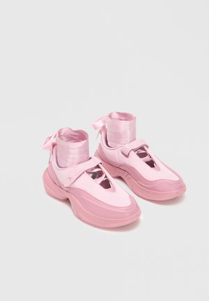 Χονδροειδή παπούτσια σε παστέλ ροζ με φαρδιές λωρίδες βέλκρο και σατέν κορδέλες που τυλίγονται γύρω από ψηλά μανίκια στον αστράγαλο σε λευκό φόντο.