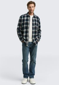 Blauwe geruite flanellen shirt met witte en rode accenten, gedragen over een wit T-shirt. Gecombineerd met blauwe denim en witte sneakers.