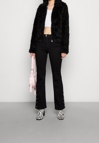 Svart fuskpälsjacka, vit crop top, svarta utsvängda jeans med knappdetaljer, och zebra-mönstrade klackstövlar; håller en rosa handväska.