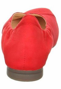 Scarpa piatta rossa con esterno in morbido camoscio, punta arrotondata e suola bassa marrone. Presenta un design a foro sul tallone per la ventilazione.