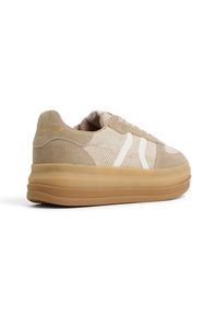 Beżowe sneakersy z teksturowanym, dzianinowym wierzchem, z zamszowymi akcentami i białymi paskami. Masywna guma podeszwa i złoty detal logo na pięcie.