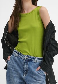 Ribbed zielony top na ramiączkach, bez rękawów, w połączeniu z jasnoniebieskimi dżinsami z wysokim stanem oraz czarną kurtką w paski.