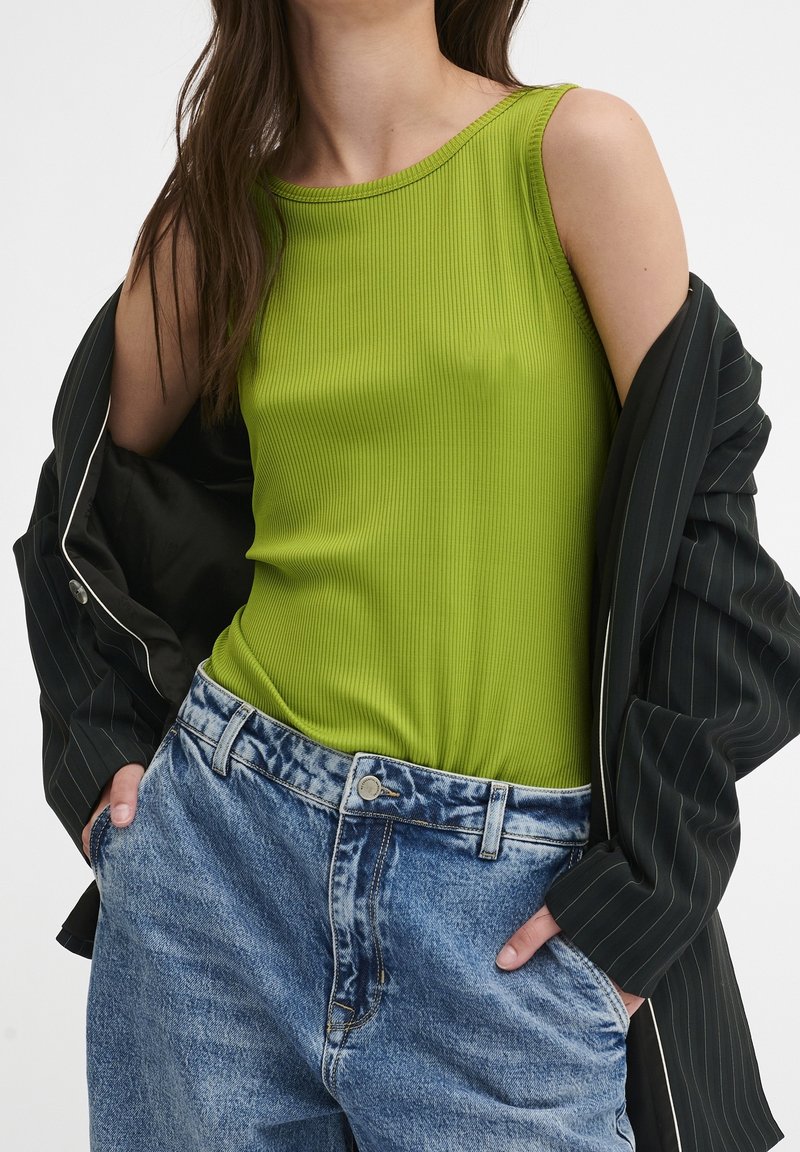 Ribbed zielony top na ramiączkach, bez rękawów, w połączeniu z jasnoniebieskimi dżinsami z wysokim stanem oraz czarną kurtką w paski.