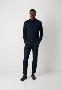 Navy pullover sweater with a mock neck, paired with dark navy chinos and black lace-up shoes. Smooth texture, fitted design.