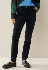 Marineblå kordfløjl-bukser med slim fit, frontlommer og en blød tekstur. Kombineret med blanke brune loafers for et raffineret look.
