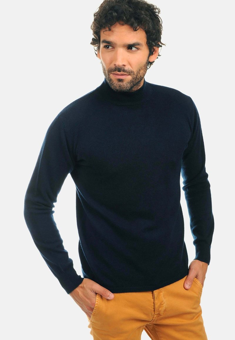 Marineblauer Rollkragenpullover aus weichem Material, mit langen Ärmeln und figurbetontem Design. Kombiniert mit hellen Hosen.