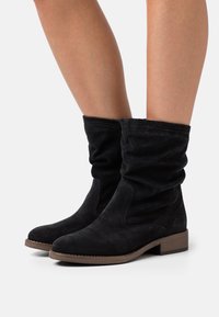 Black suede ankle boots with a slouchy design, round toe, and low block heel; features contrasting stitching and side accents.