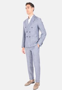 Abito doppiopetto a righe blu e bianche con rever a contrasto, tessuto testurizzato, pantaloni coordinati e mocassini marrone chiaro.