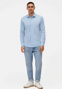 Camicia azzurro chiaro in cotone con collo classico e maniche lunghe. Abbinata a jeans in denim chiaro e sneaker bianche.