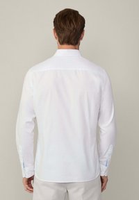 Witte blouse met lange mouwen en knoopmanchetten, met een klassieke kraag en gladde stof. De achterkant toont een getailleerde silhouette en nette naden.
