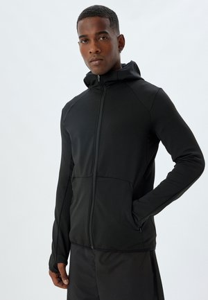 Black zip-up jacket with a hood, features smooth fabric, fitted design, thumbholes in sleeves, and front pockets.
