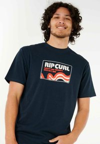 Camiseta de algodón azul marino con un gráfico de estilo retro que incluye "RIP CURL" y acentos ondulados en rojo y blanco. Diseño de manga corta y cuello redondo.