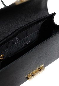 Borsa nera testo con chiusura in metallo dorato, dotata di una tasca interna con zip e foderata in tessuto liscio.