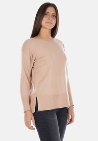Maglione in maglia beige con vestibilità rilassata e spacchi laterali, scollatura rotonda e dettagli a coste sull'orlo e sui polsini, abbinato a jeans scuri.