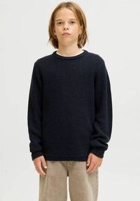Dunkelblauer Strickpullover mit Rundhalsausschnitt und langen Ärmeln. Verfügt über ein strukturiertes Muster sowie gerippte Bündchen und Saum. Getragen über hellbraunen Hosen.