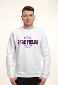 Sweatshirt blanc avec col rond et manches longues, arborant le texte brodé en violet "PARK FIELDS ATHLETICS" et un emblème graphique.