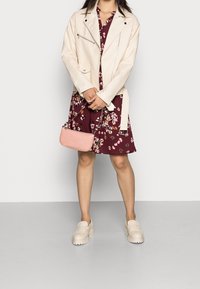 Beige konstläderjacka med dragkedjor, blommig maroon klänning, ljusrosa axelväska och beige plattform loafers.