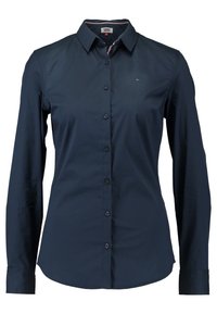 Granatowa koszula z długim rękawem, zapinana na guziki, z kołnierzykiem w kształcie ostrego wierzchołka, z akcentem w postaci logo i gładką bawełnianą strukturą. Klasyczny krój.