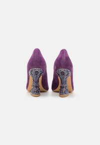 Tacchi alti in suede viola con punta affusolata e tacco decorativo impreziosito da gioielli con pietre di diverse dimensioni nelle tonalità di viola.