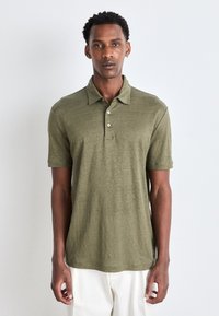 Olivgrön polo skjorta i ett texturerat tyg med en tre-knapps knäppning, korta ärmar och en avslappnad passform. Har en rak nederkant.