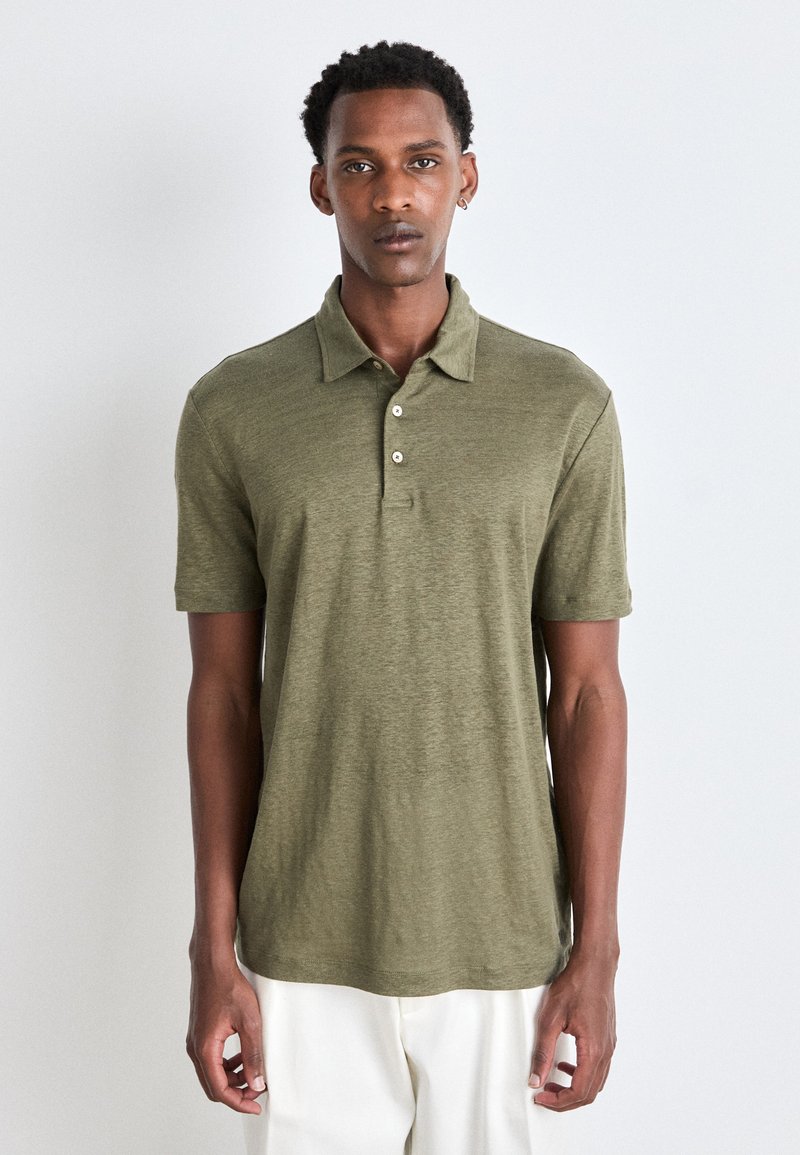 Olivgrön polo skjorta i ett texturerat tyg med en tre-knapps knäppning, korta ärmar och en avslappnad passform. Har en rak nederkant.