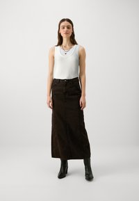 Hvit ribbet tanktopp lagd over en brun denim maxiskjørt med rett snitt. Brukt med svarte høye støvler. Enkle sølv smykker som aksenter.