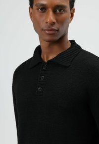 Zwarte gebreide trui met een geribde kraag, een drieknopensluiting en een gestructureerde stof. Casual pasvorm met een zachte uitstraling.