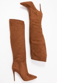 Bruine suède kniehoogte laarzen met een spitse neus en een stiletto hak. Ze hebben een gladde textuur en een strakke pasvorm.