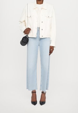 Person wearing cream jacket, light blue cropped jeans with frayed hems, black pointed heels, and holding small black quilted purse.