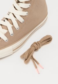 Baskets montantes en toile beige avec lacets blancs et œillets argentés, dotées d'un embout en caoutchouc et d'un lacet beige noué aux extrémités roses.