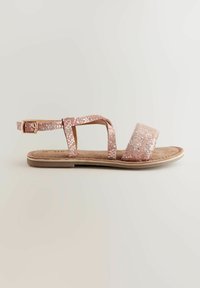 Rosa-guld sandaler med texturerade remmar, med en spänne vid vristen och en vadderad sula, placerade på en platt, neutralt färgad sula.