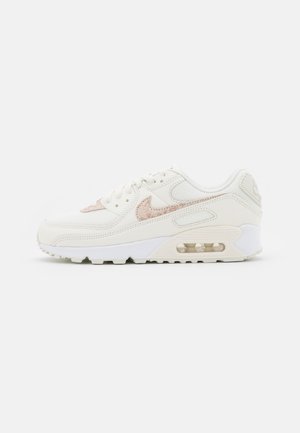 Baskets blanches avec motif beige en peau de serpent, logo Nike Swoosh, coussin d’air visible dans la semelle et détails texturés sur la tige et le talon.