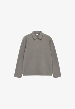 Szara koszulka polo z długim rękawem, wykonana z dzianiny wafelowej, z kołnierzykiem i dwuprzyciskowym dekoltem, rozłożona na płasko na białym tle.