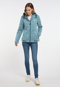 Blåmelerad jacka med dragkedja, huva och dragsko. Strukturerad tyg, sidofickor med knappstängning, bärs över en vit topp.