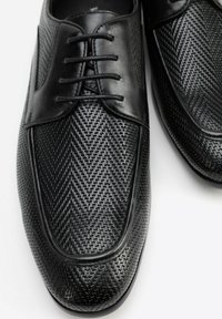 Scarpe nere formali realizzate in materiale tessuto con motivo intrecciato e dettagli in pelle liscia. Presentano una punta rotonda e un classico design con lacci.