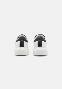 White sneakers with a black leather heel counter, embossed logo on the back, and a textured rubber sole. Simple design, modern aesthetic.