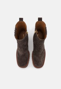 Botas de tobillo de ante marrón con un acabado suave, que presentan un cierre lateral con cremallera y un panel trasero texturizado. Interior de cuero con una suela cosida.