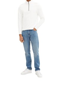 Sudadera blanca con cremallera y textura acanalada, combinada con jeans de mezclilla azules y zapatillas blancas. Diseño simple, jeans de corte recto, look casual.