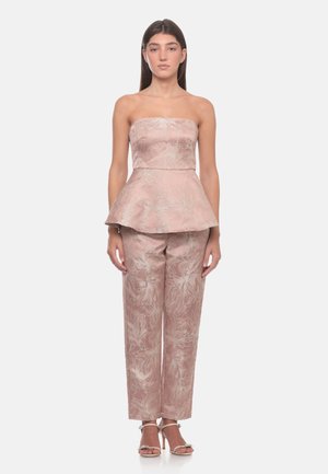 Donna che indossa un top peplum in jacquard floreale rosa senza spalline e pantaloni dritti abbinati con sandali con tacco aperto.