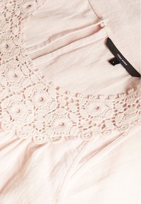Blusa rosa chiaro con ricami floreali attorno al colletto, con pieghe nella parte inferiore. Insegna visibile con il nome del marchio "Vero Moda" e la taglia "S."