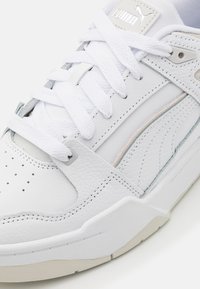 Hvide lædersneakers med struktureret overflade, der har snørehætte, diskrete grå og pink accenter samt perforeringer på tåhætten.