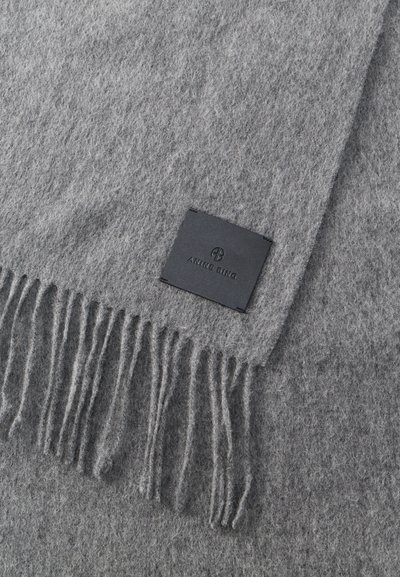 Puha szürke gyapjúsál rojtos végekkel és egy fekete, téglalap alakú címkével, amelyre az "ANINE BING" márkanév van domborítva, varrva.