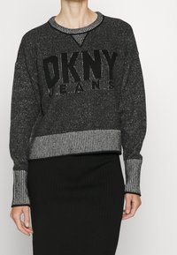 Svart och grå stickad tröja med en framträdande "DKNY JEANS" logotyp på framsidan. Har en randig ribbad nederkant och manschetter, samt rund halsringning.