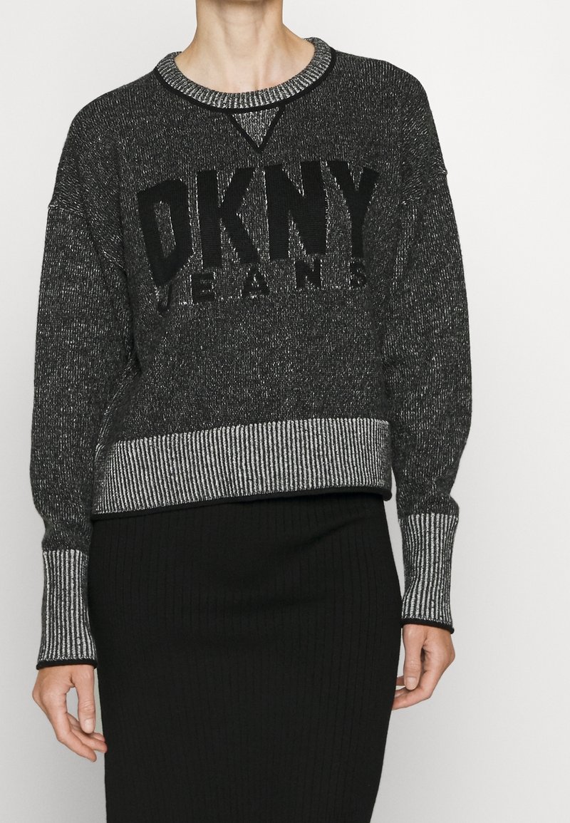 Svart och grå stickad tröja med en framträdande "DKNY JEANS" logotyp på framsidan. Har en randig ribbad nederkant och manschetter, samt rund halsringning.