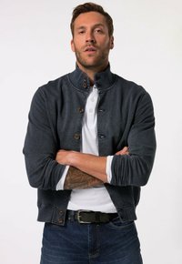 Dark denim jacket with a high collar, brown buttons, and ribbed cuffs, layered over a white polo shirt, paired with blue jeans.