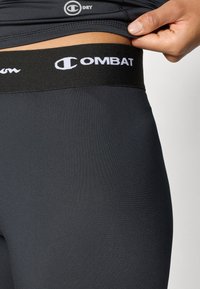 Czarne legginsy sportowe o gładkiej fakturze i elastycznym pasku w talii, z białym logo "COMBAT". Idealne do aktywności fizycznej.