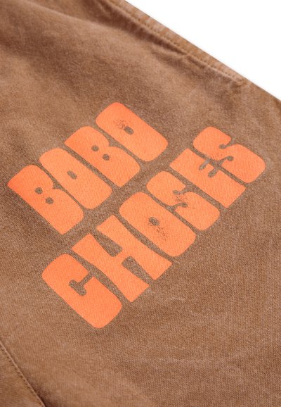Brown fabric featuring bold orange text reading "BOBO CHOSES," with a textured finish and visible stitching details.