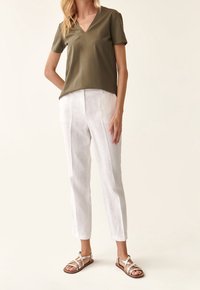 Olivově zelený krátký rukáv V-krk top v kombinaci s bílými lněnými kalhotami a plochými páskovými sandály. Tento outfit spojuje světlé a neutrální tóny.