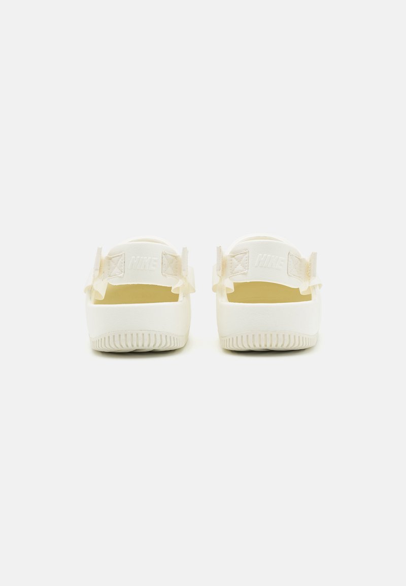 Sandalias Nike blancas con parte trasera abierta, suelas de goma texturizadas y detalles de logo en relieve en las correas. Material suave, diseño minimalista.